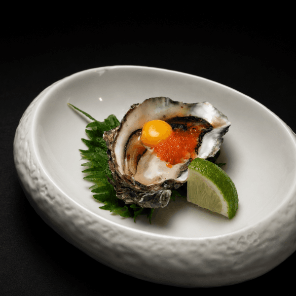 Oyster with roe, egg yolk, and lime in a white bowl